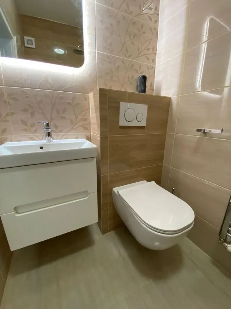 Inštalácia zaveseného WC a umývadla v modernej kúpeľni s obkladom v prírodných tónoch.