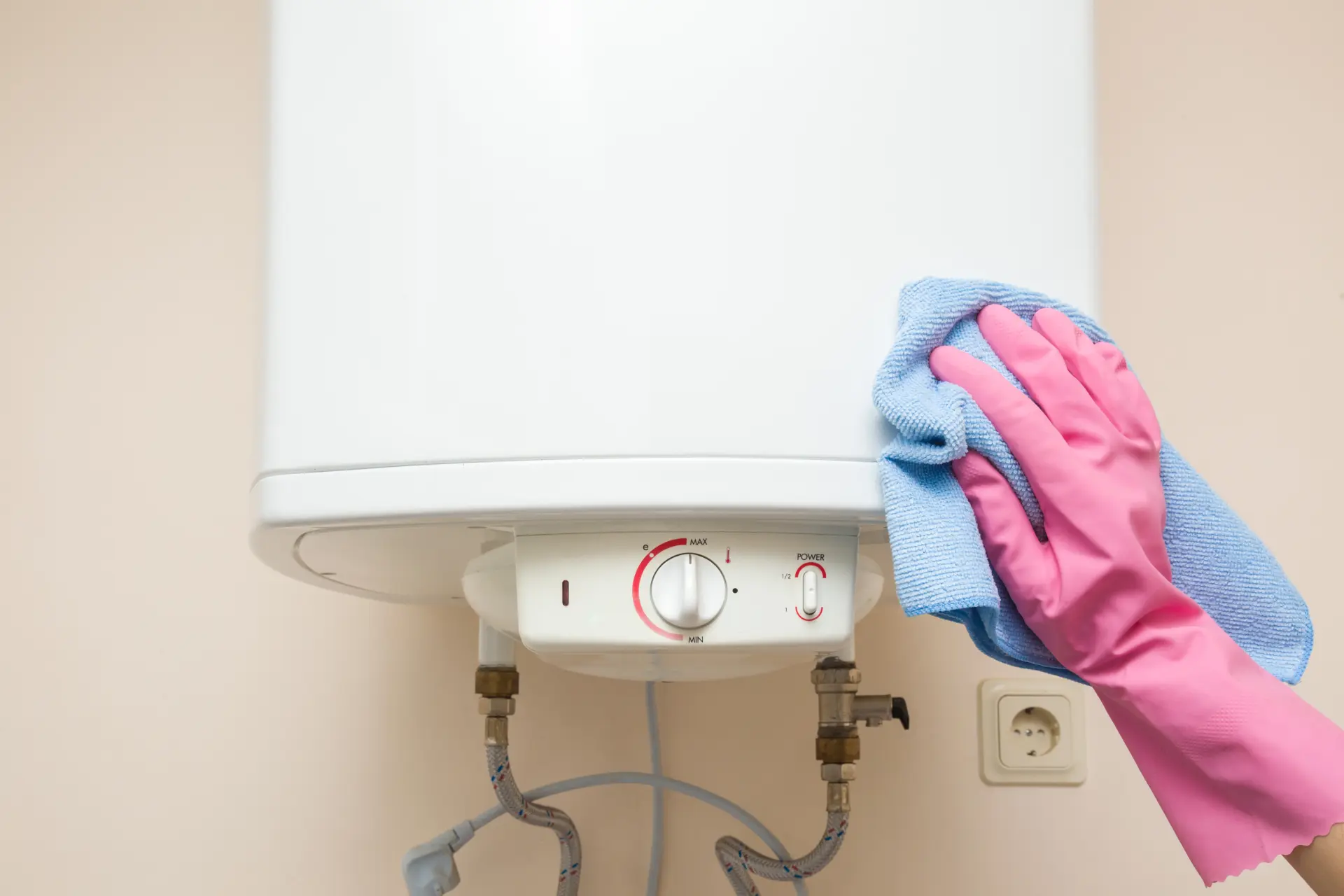 Ruka v gumovej rukavici čistí povrch elektrického bojlera jemnou handričkou na udržanie hygieny.