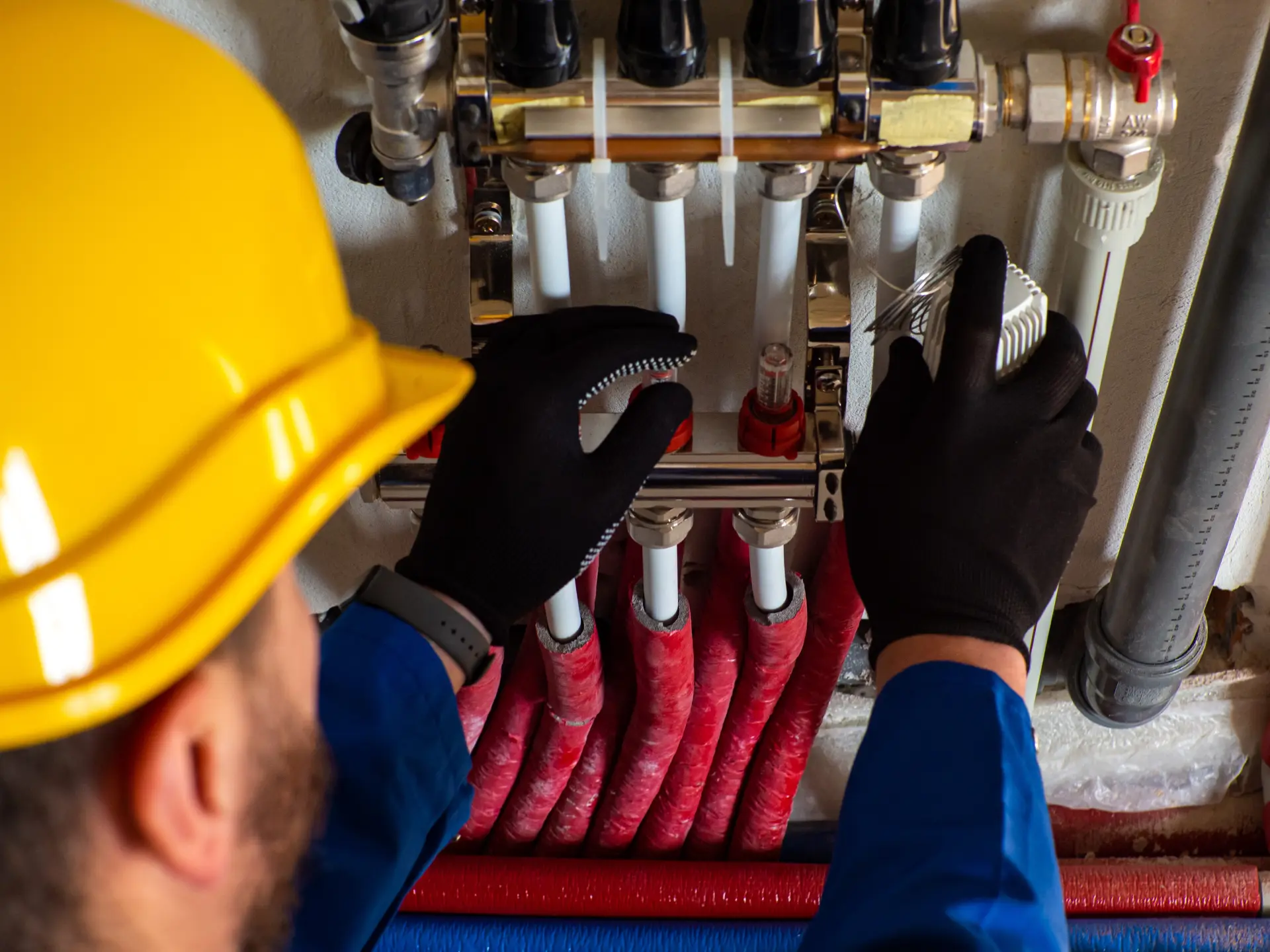 Technik kontroluje rozvádzač podlahového kúrenia s viacerými hadicami, ventilmi a pripojeniami.