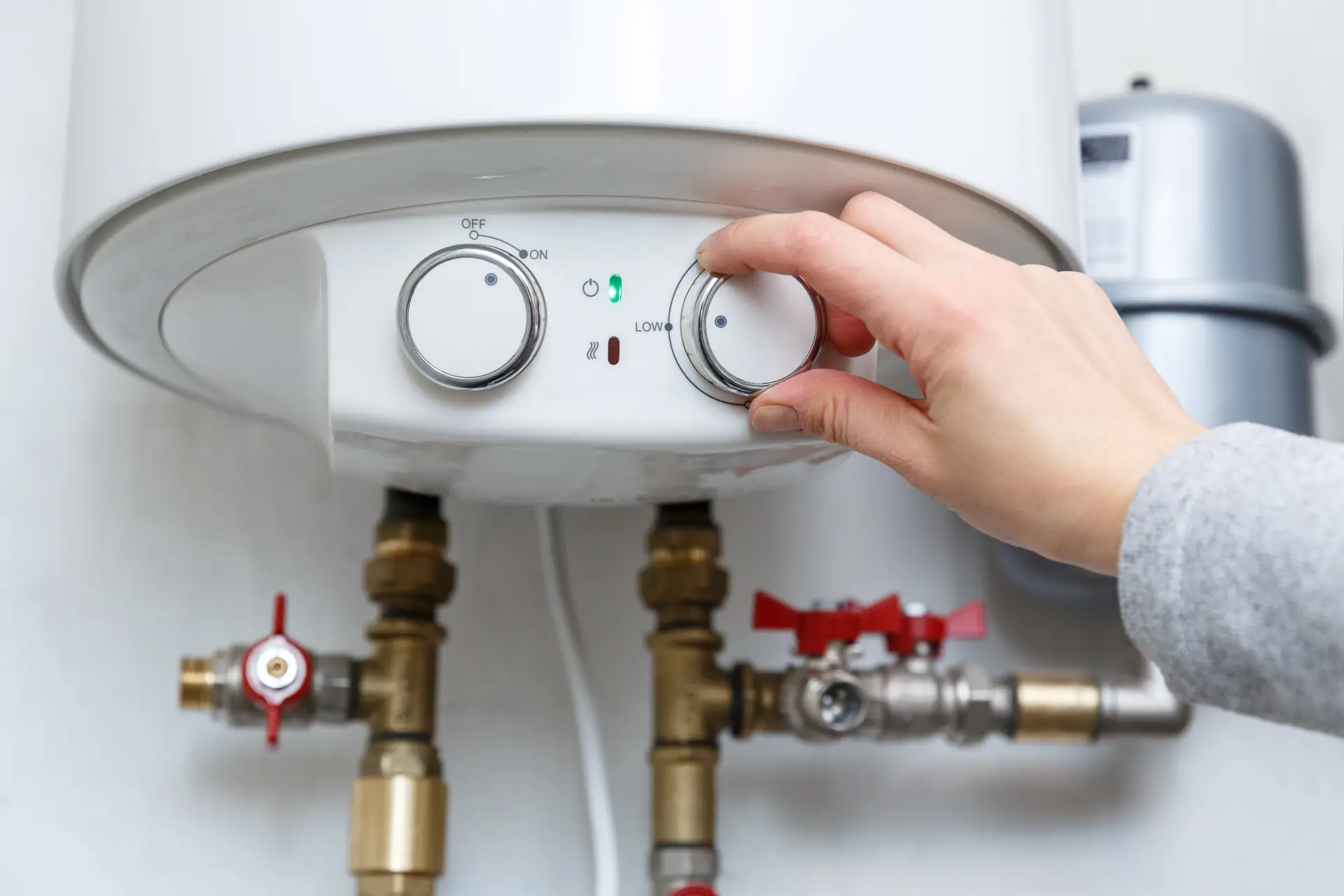 Ruka otáča termostatický regulátor na elektrickom bojleri pre nastavenie požadovanej teploty vody v domácnosti.