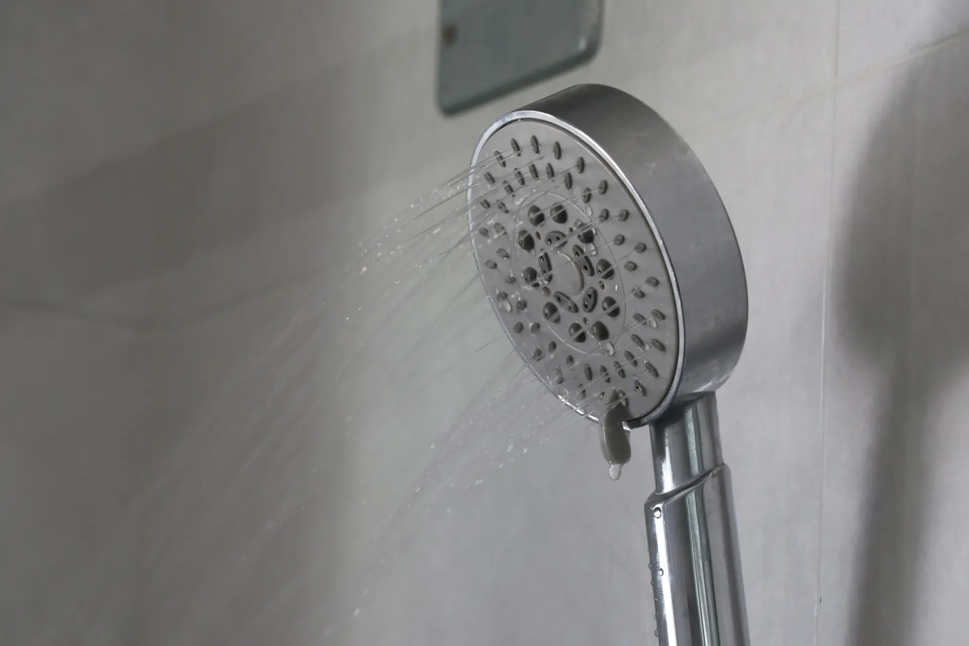 Detail modernej ručnej sprchovej hlavice so slabým prúdom vody, ktorá naznačuje možnú potrebu čistenia alebo odvápnenia sprchového systému.