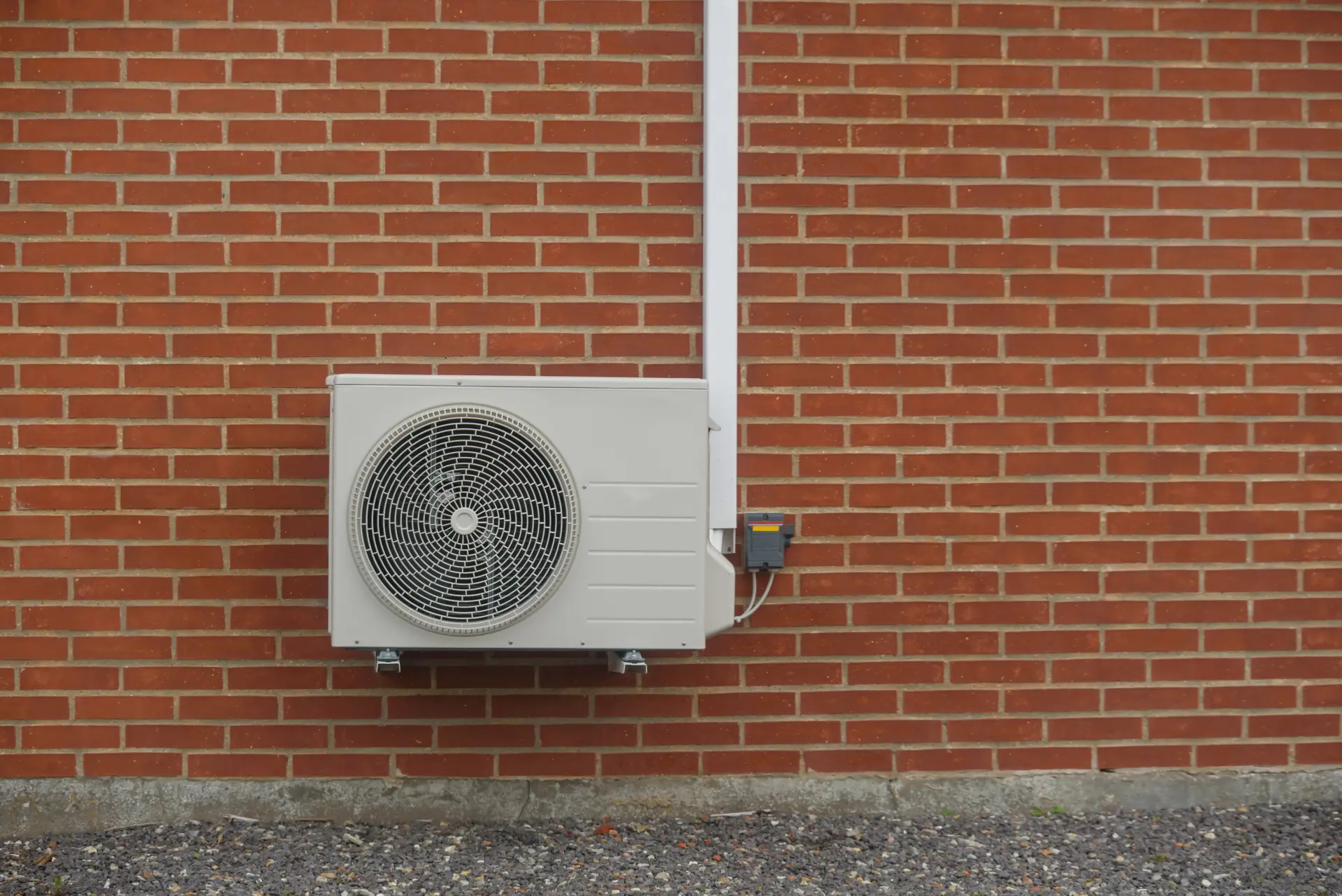 Tepelné čerpadlo nainštalované na červenej tehlovej fasáde rodinného domu s elektrickým napájaním.
