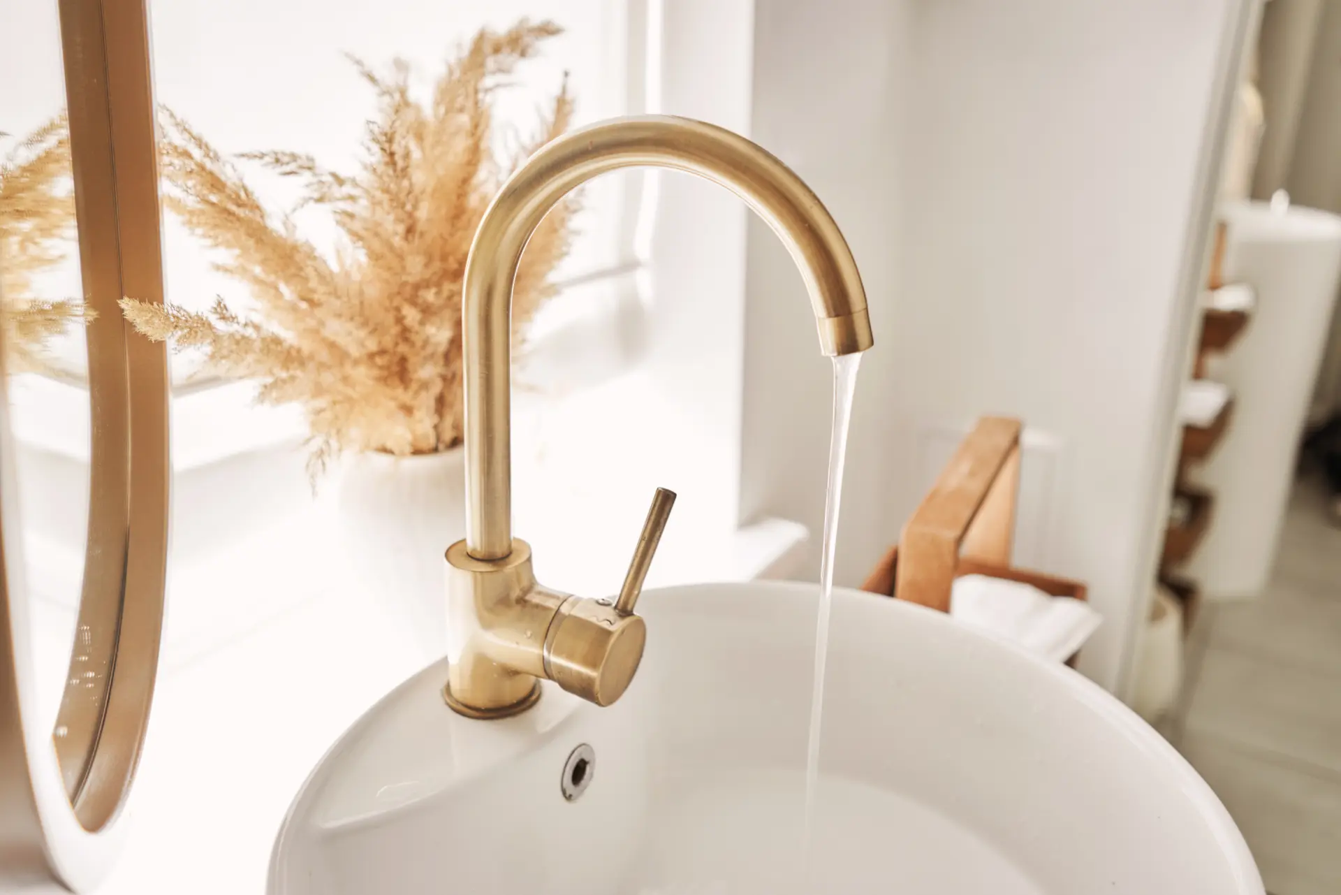 Elegantní zlatá vodovodní baterie s tekoucí vodou umístěná na bílém umyvadle.