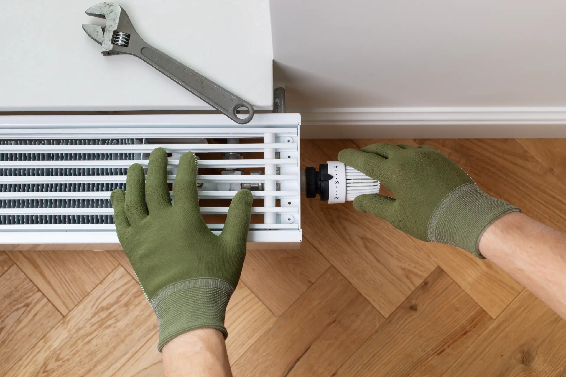 Nastavenie termostatickej hlavice radiátora rukou v ochranných rukaviciach.