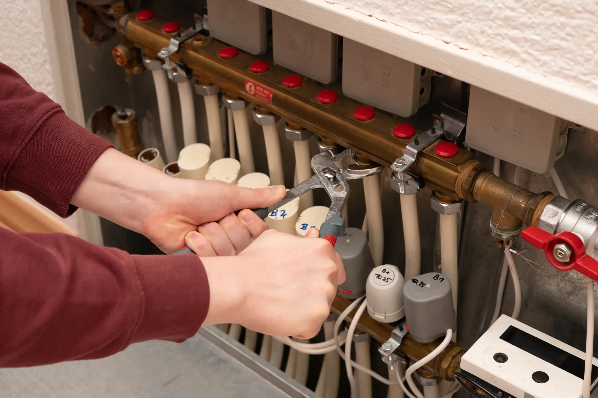 Technik uťahuje spoje na rozdeľovači podlahového kúrenia pomocou kľúča.