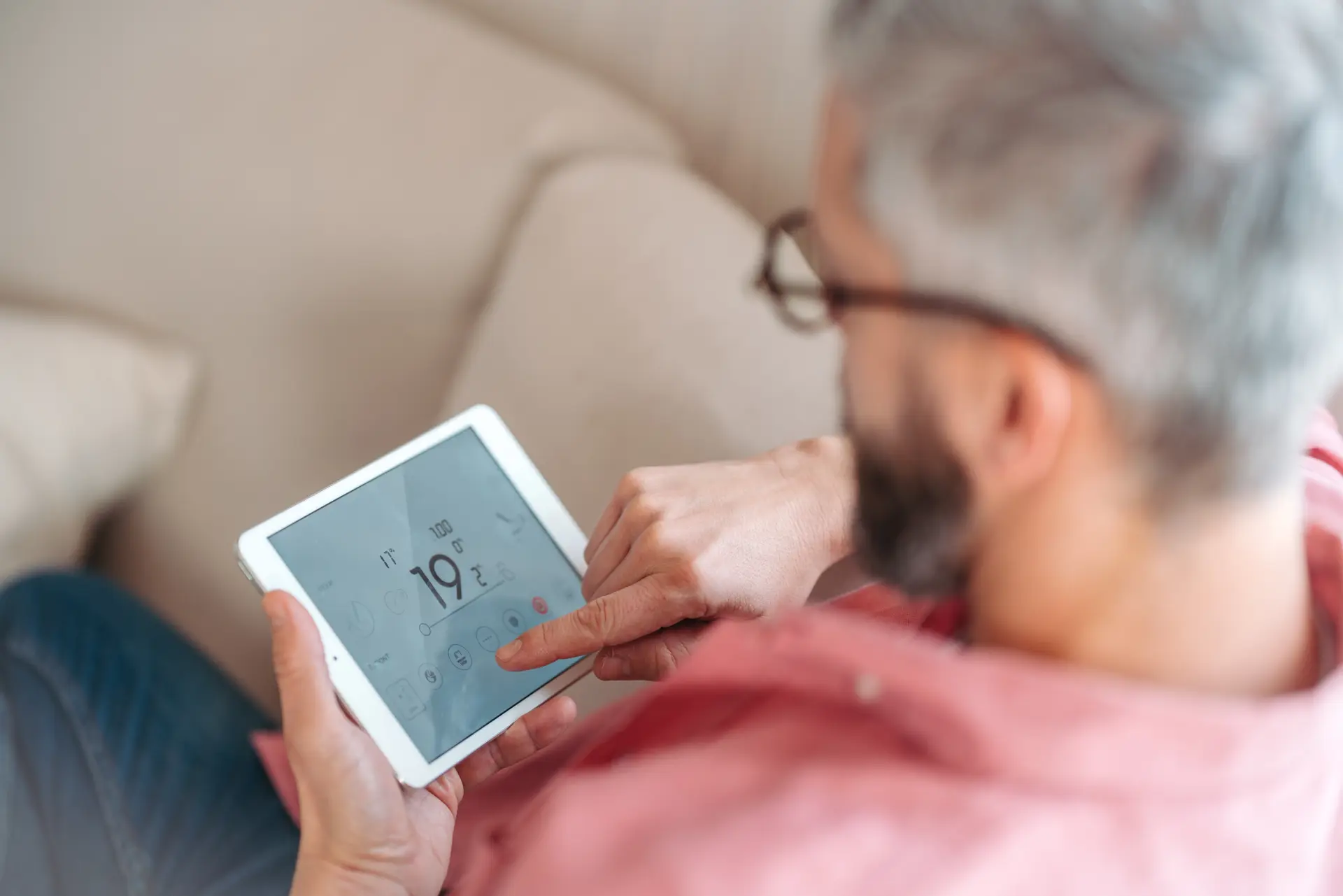 Muž ovláda smart termostat na tablete a nastavuje teplotu v domácnosti.