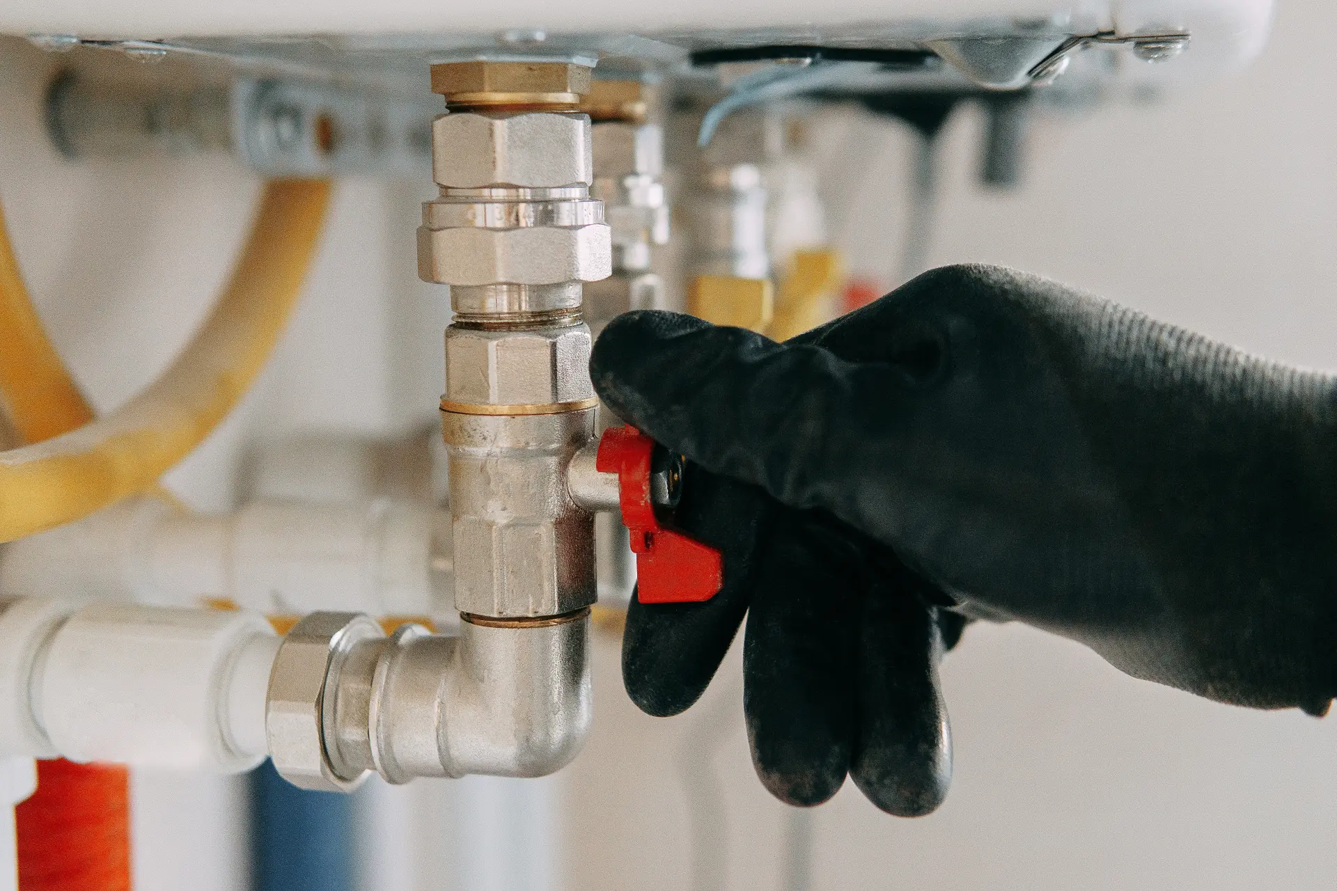 Inštalatér v rukaviciach otáča uzatvárací ventil na potrubí pod umývadlom pri oprave alebo údržbe vodovodného systému.