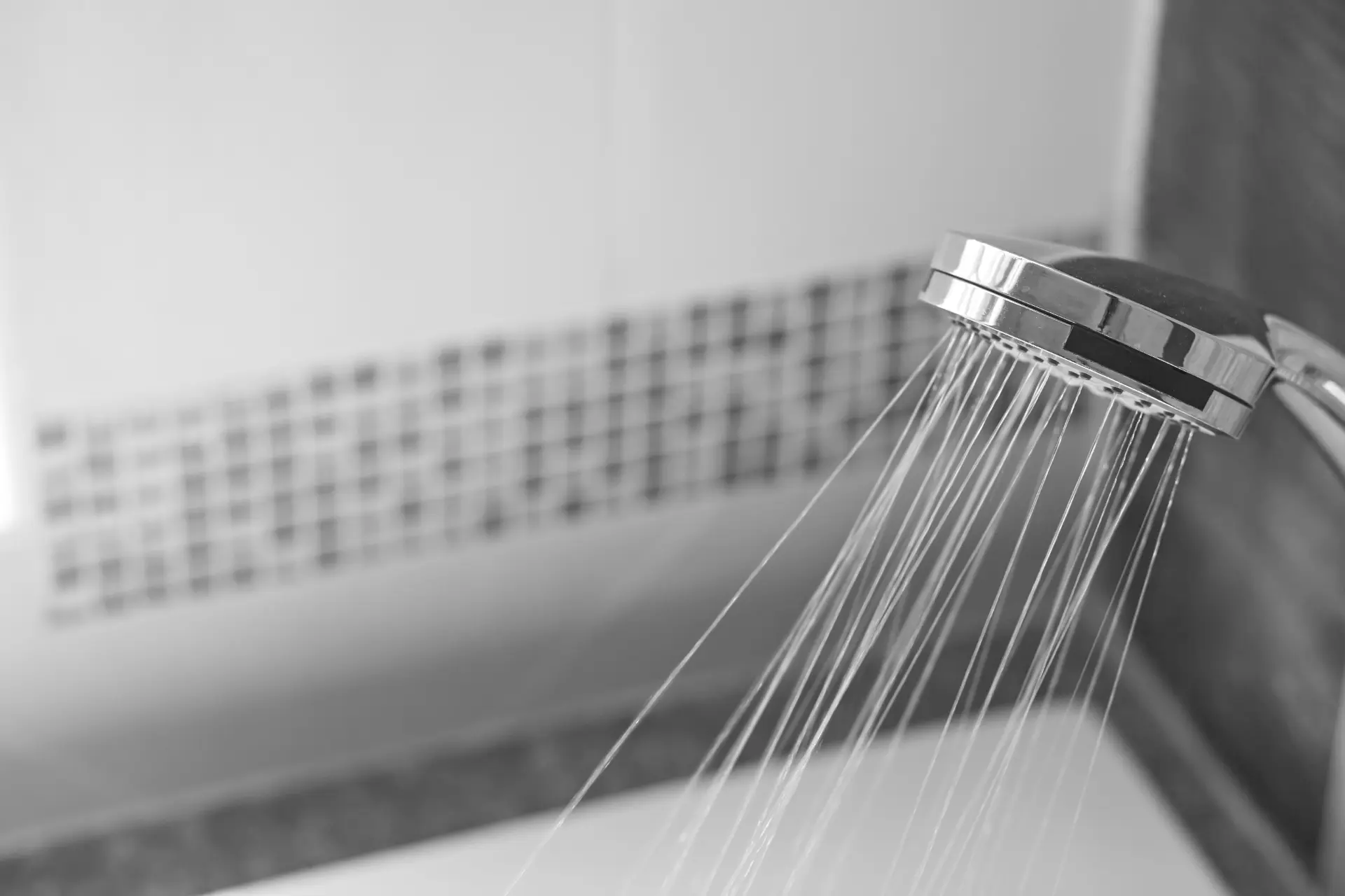 Čiernobiely detail sprchovej hlavice s tečúcou vodou v kúpeľni.