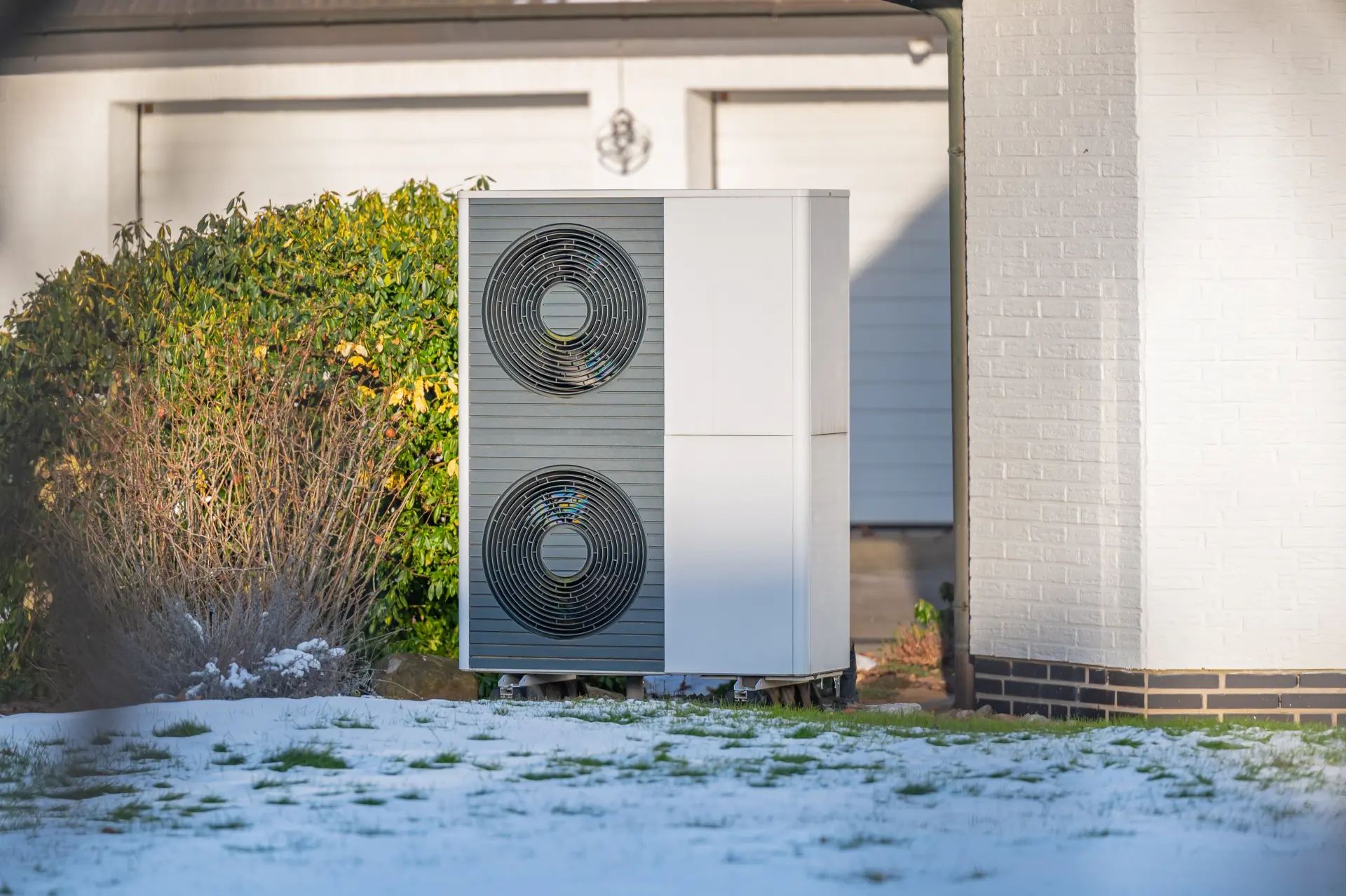 Vonkajšia jednotka tepelného čerpadla pri rodinnom dome počas zimného obdobia.
