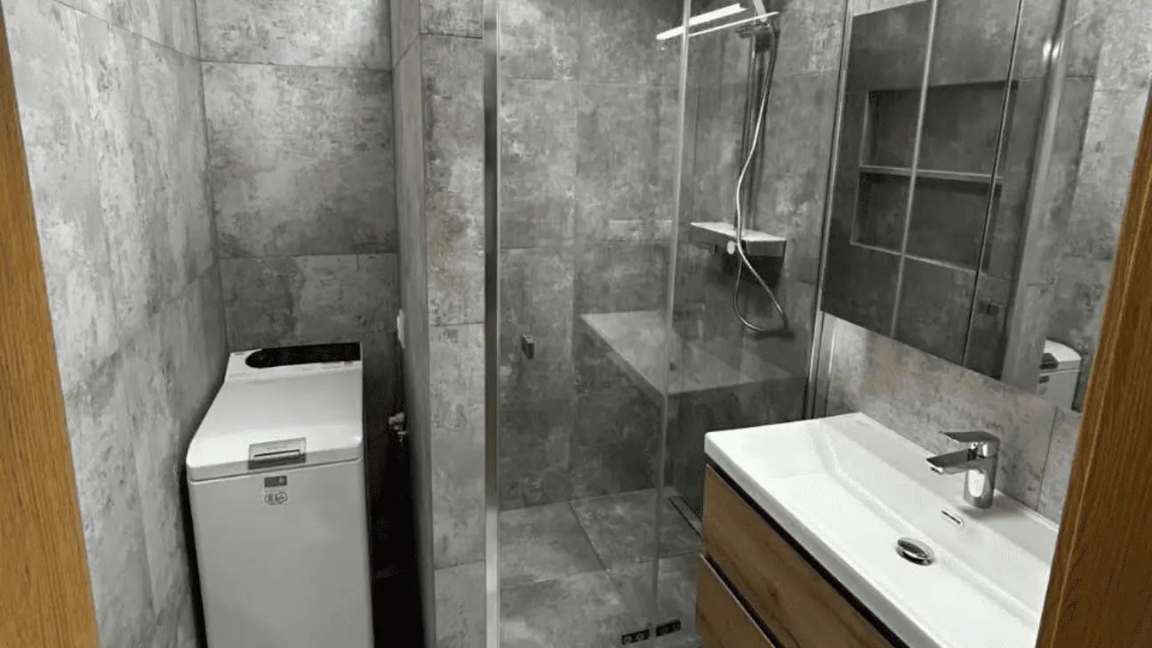 Kompletne dokončená kúpeľňa v sivom štýle so sprchovým kútom, umývadlom a sanitárnymi rozvodmi.